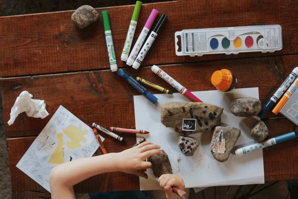 Criança se diverte e aprende com jogos e brincadeiras na Educação Infantil usando tintas, papel, giz de cera, canetinhas hidrocor e pedras de jardim.