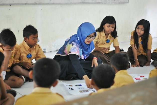 Uma professora mostra atividade baseada em problema sentada no chão com os alunos ao seu redor.