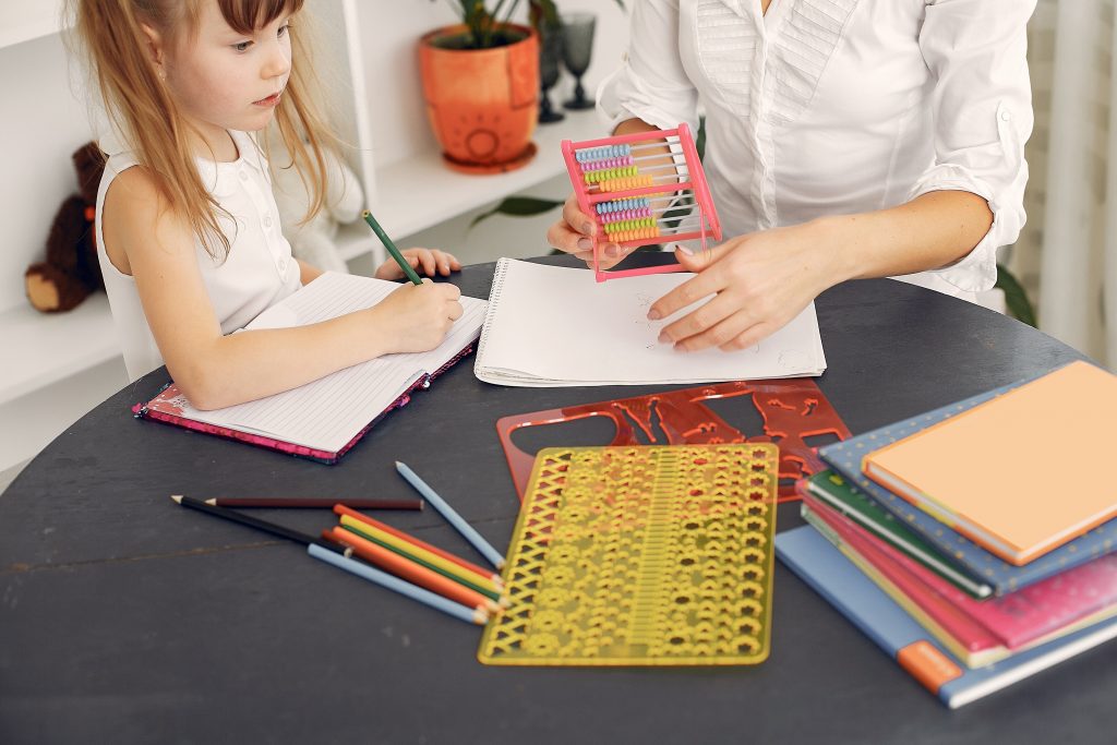 Uma menina interagindo com diferentes materiais didáticos: livros, ábaco e réguas geométricas.