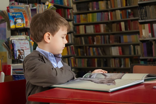 Uma criança sentada dentro de uma biblioteca pequena lê um livro, ilustrando o aprendizado de matemática na Educação Infantil.
