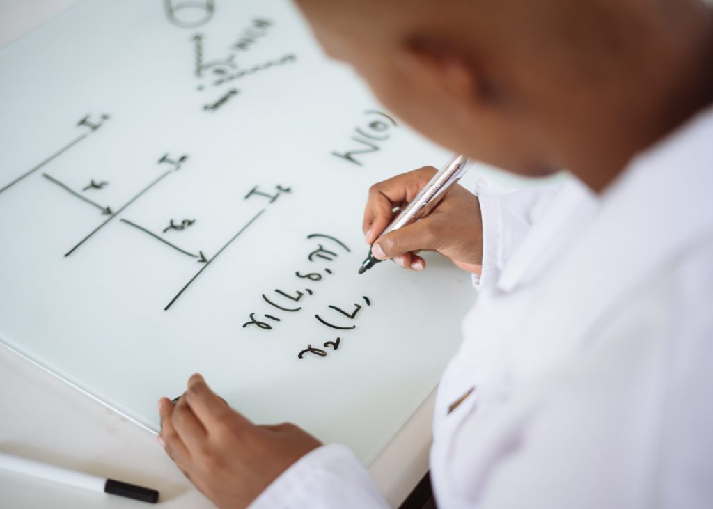 Estudante escrevendo fórmulas matemáticas em um quadro branco, em um exemplo mais tradicional da matemática lúdica.