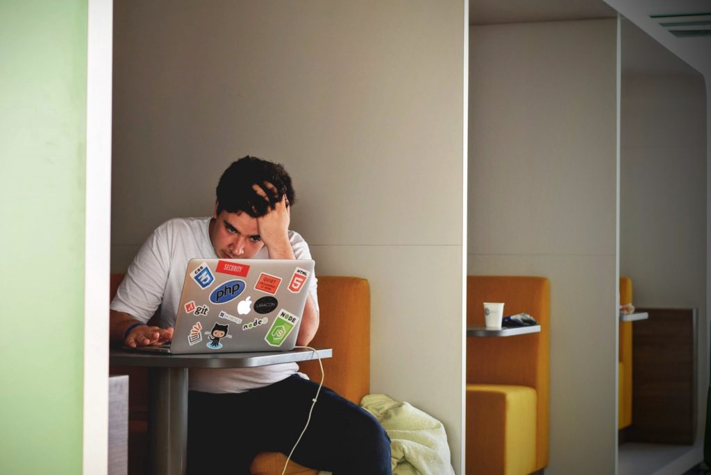 Um rapaz adolescente estudando em livro didático ensino médio no computador, em aulas on-line.