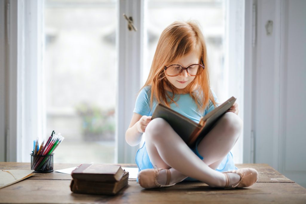 Menina lendo livros didáticos Ensino Fundamental sentada de pernas cruzadas. 