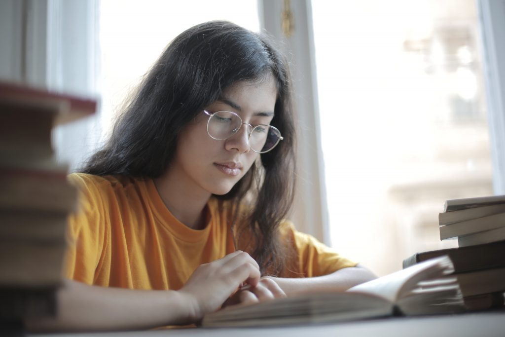 Jovem adolescente mulher lendo livros didáticos Ensino Fundamental.