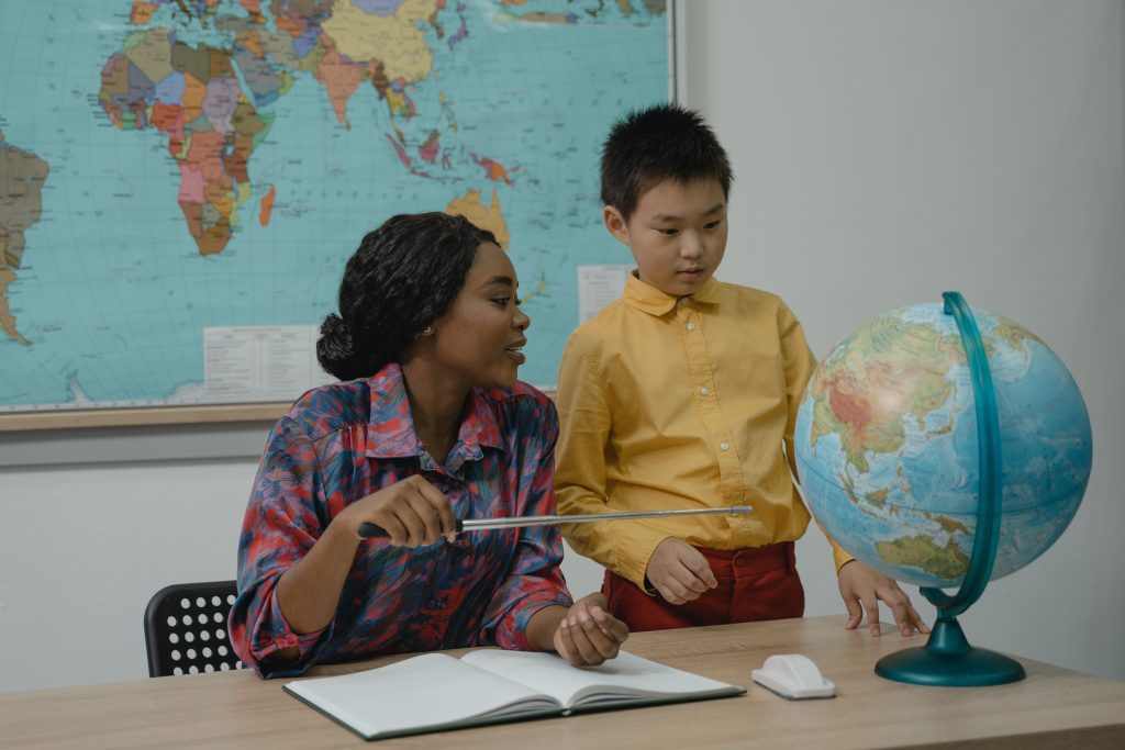 Professora ajudando aluno a estudar geografia, como exemplos de práticas inclusivas na escola.