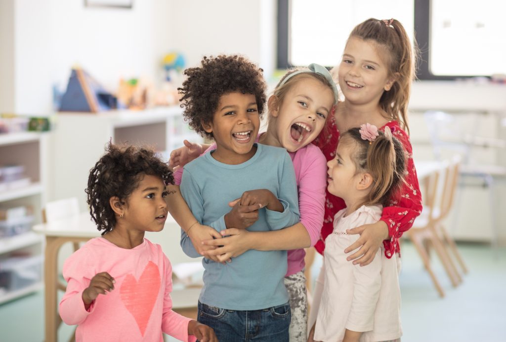 Crianças (1 menino e 4 meninas) se abraçando e demonstrando a importância de desenvolver a inteligência emocional na escola. 