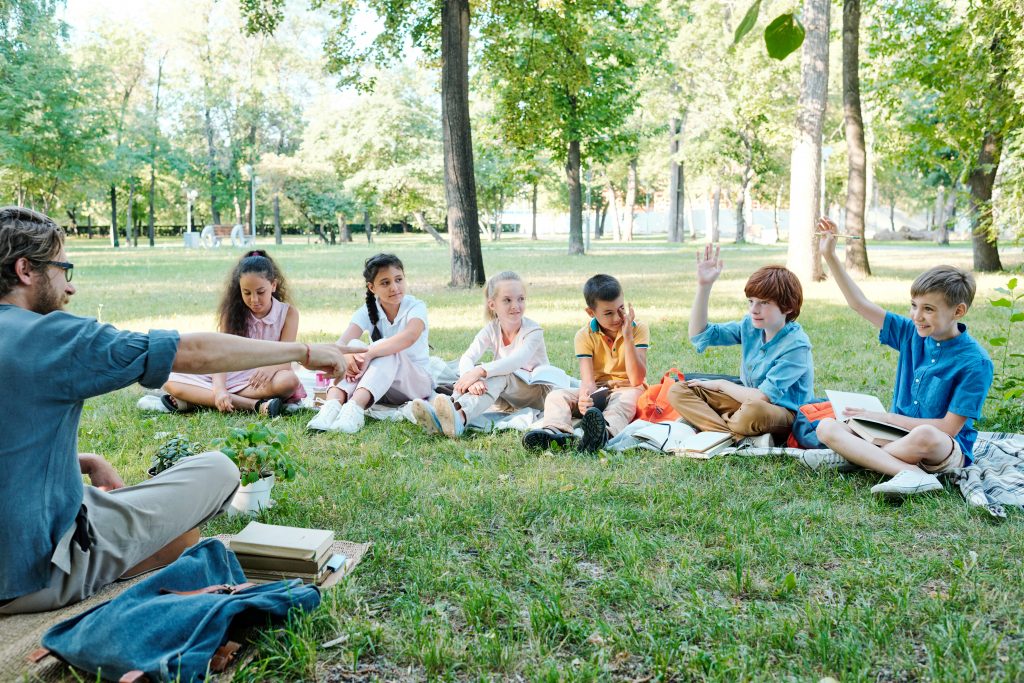 Crianças em roda ao ar livre, conversando sobre suas experiências de vida em dinâmica de inteligência emocional na escola. 