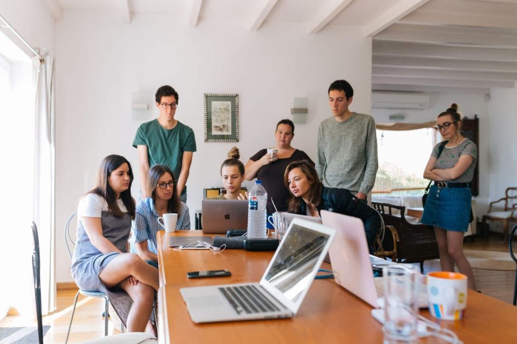 Grupo de pessoas cercadas em volta de uma mesa, olhando em um notebook. A imagem representa um grupo de docentes trabalhando em conjunto para projetos multidisciplinares